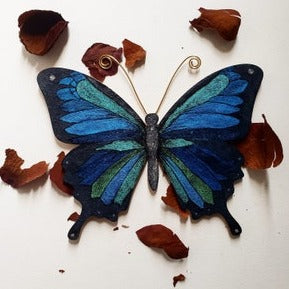 painted wooden Blue butterfly with green accents and scattered leaves on a white background