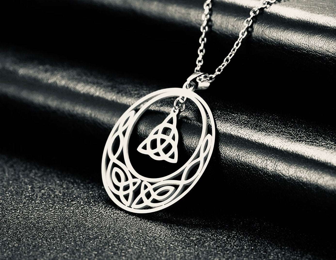 Silver necklace with a intricate Celtic knot pendant and center charm on a dark textured surface