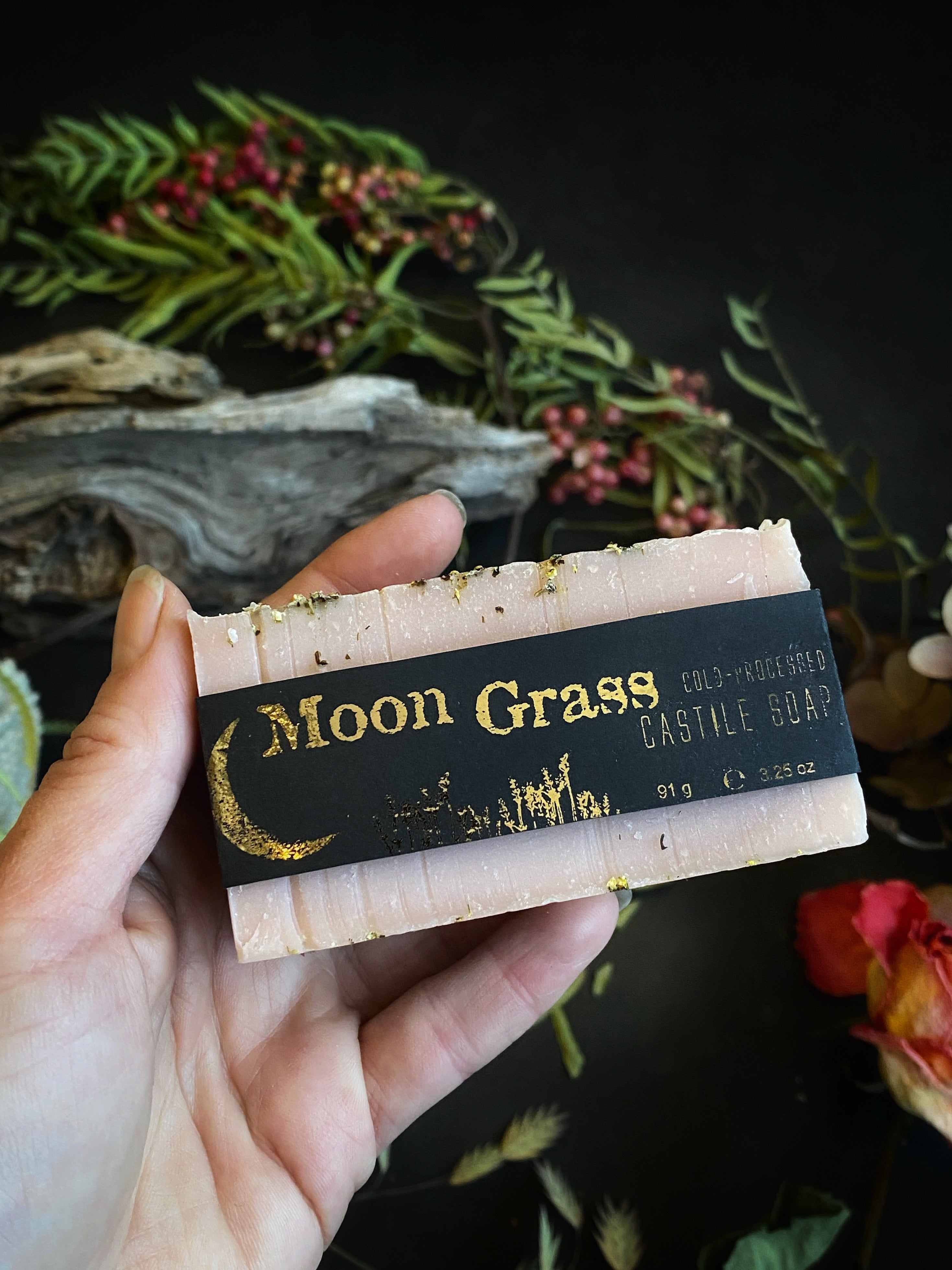 Hand holding a bar of Moon Grass Artisan Castile Soap with label against natural background