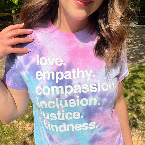 Woman wearing tie-dye shirt with love empathy compassion inclusion justice kindness text outdoors - inspirational graphic tee