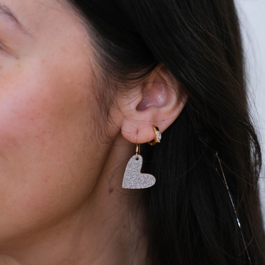 Close-up of a person wearing sparkling silver heart-shaped earrings