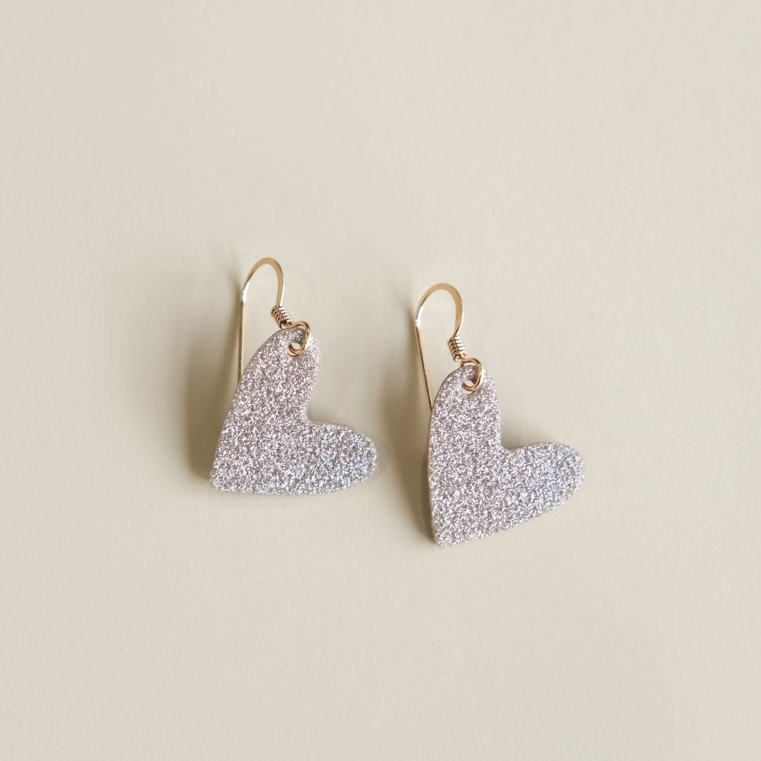 Heart-shaped earrings with glittery champagne finish on a beige background