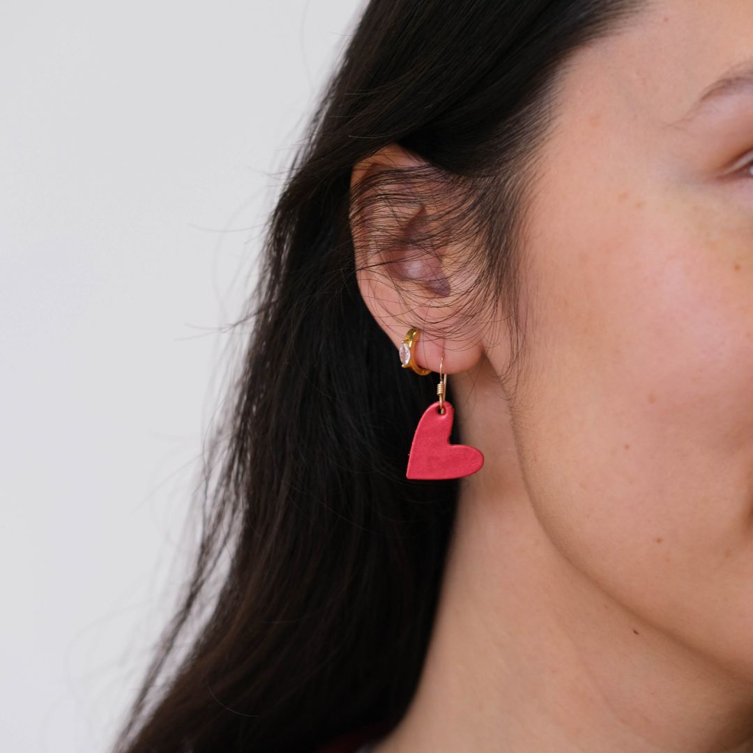 Close-up of a person wearing a red heart-shaped earring against a white background