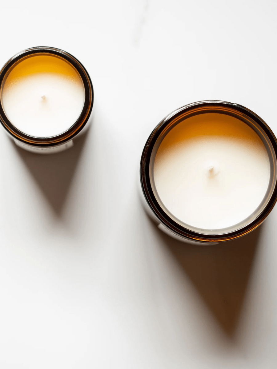 Two Alchemist + Co. wellness candles in amber glass containers on white background top view - aromatherapy candles