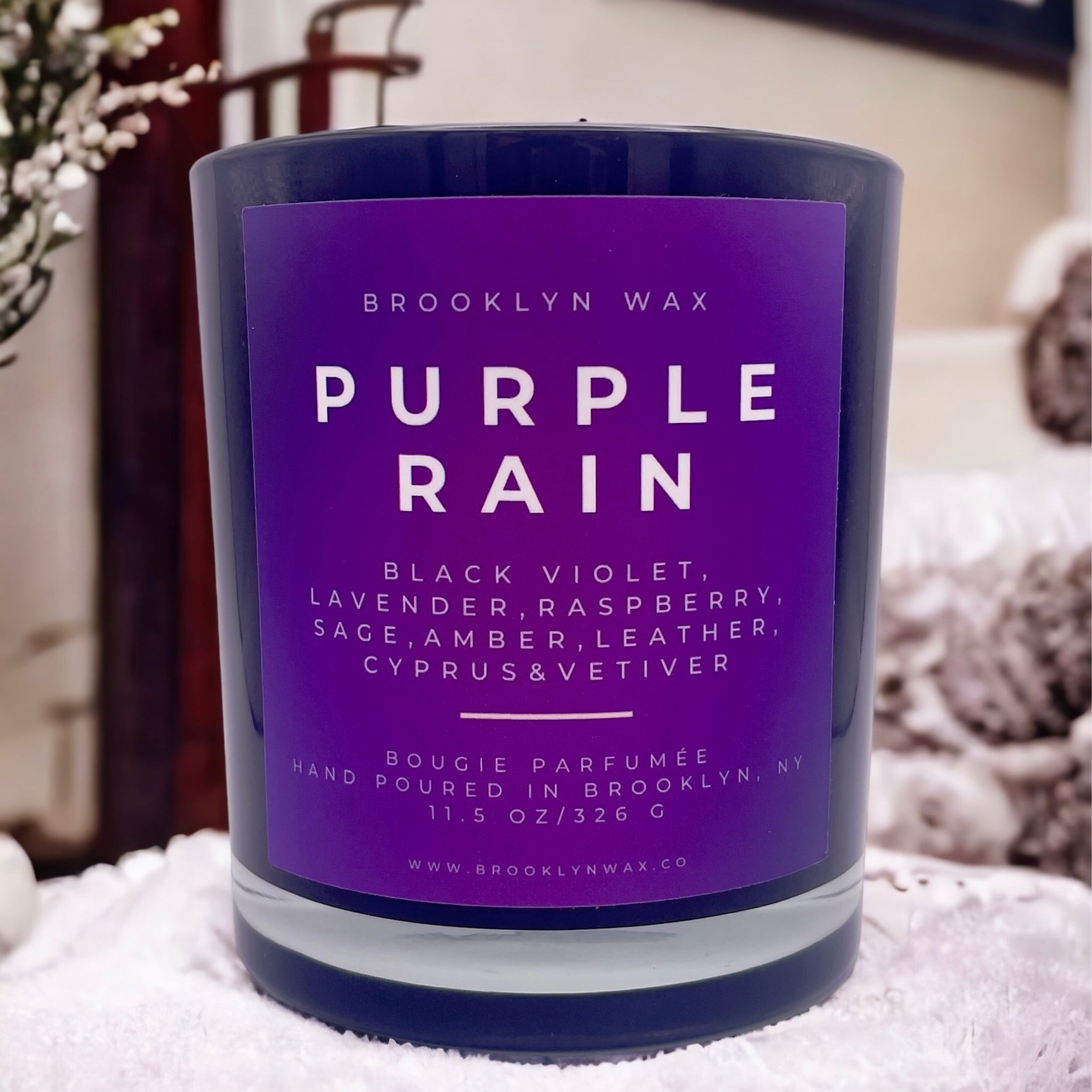 Purple Rain candle by Brooklyn Wax on white surface with plants in background