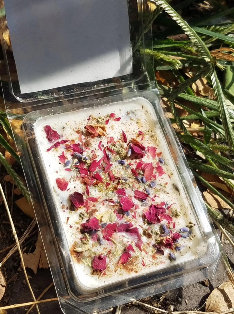 Rectangular wax melt with dried flowers on top in a clear container on grass