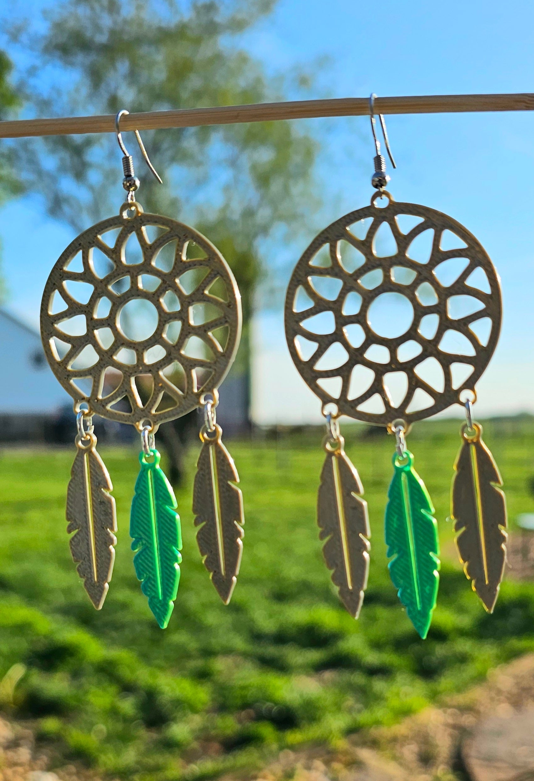 Dreamcatcher earrings with feathers hanging on rod against blurred natural background - made in America boho jewelry