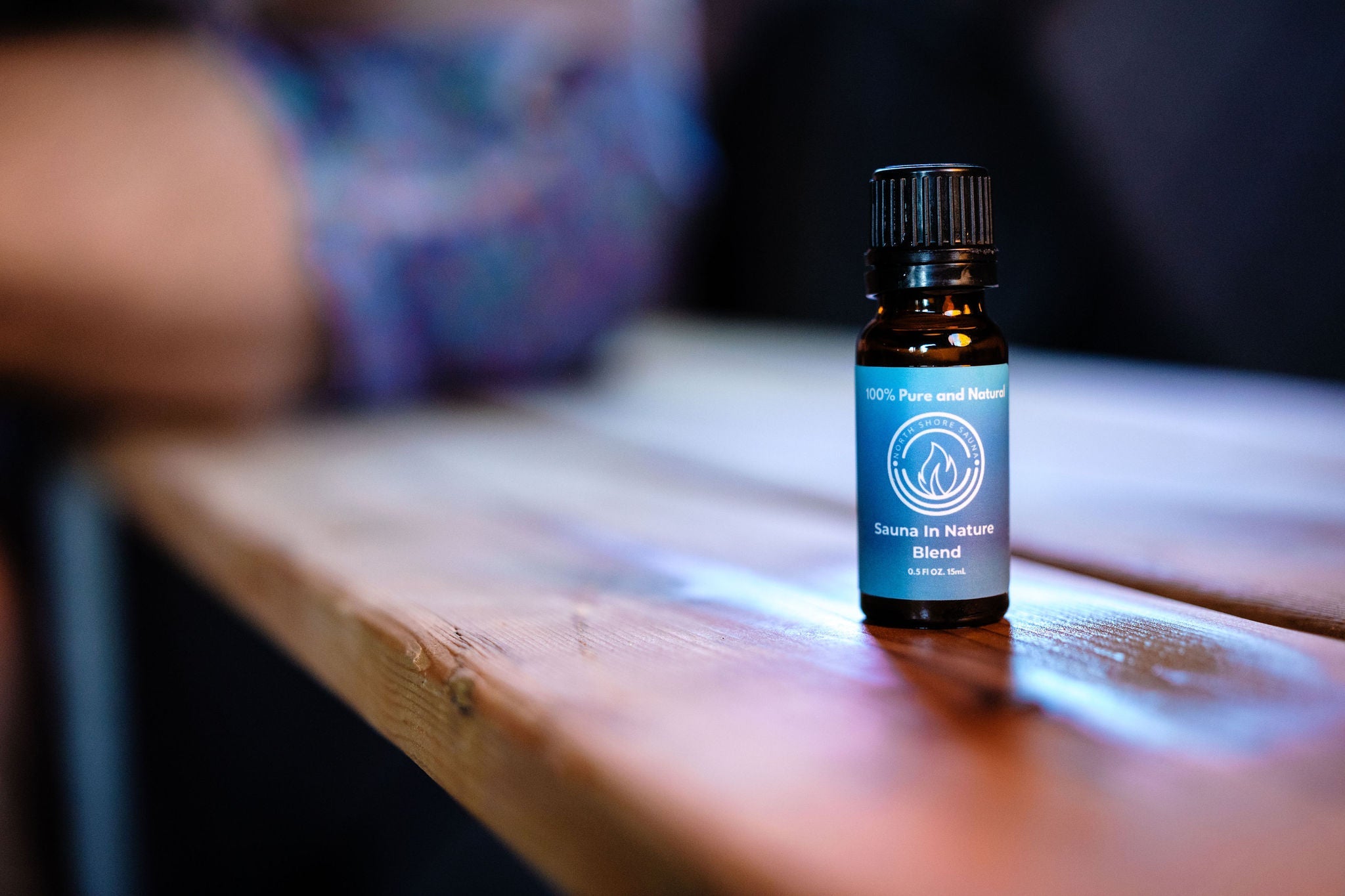 Brown essential oil bottle with blue label on a wooden surface with a blurred background
