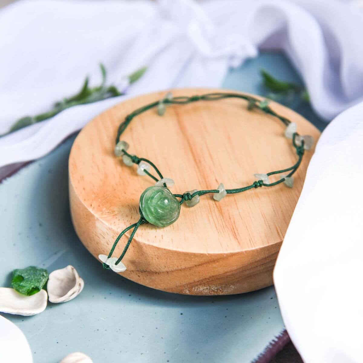 green cord anklet with green adventurine beads and large green rose-shaped focal bead on a wooden coaster