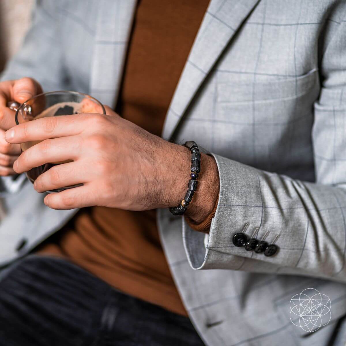 Person in gray suit wearing black spiritual protection bracelet holding drink - energy protection jewelry