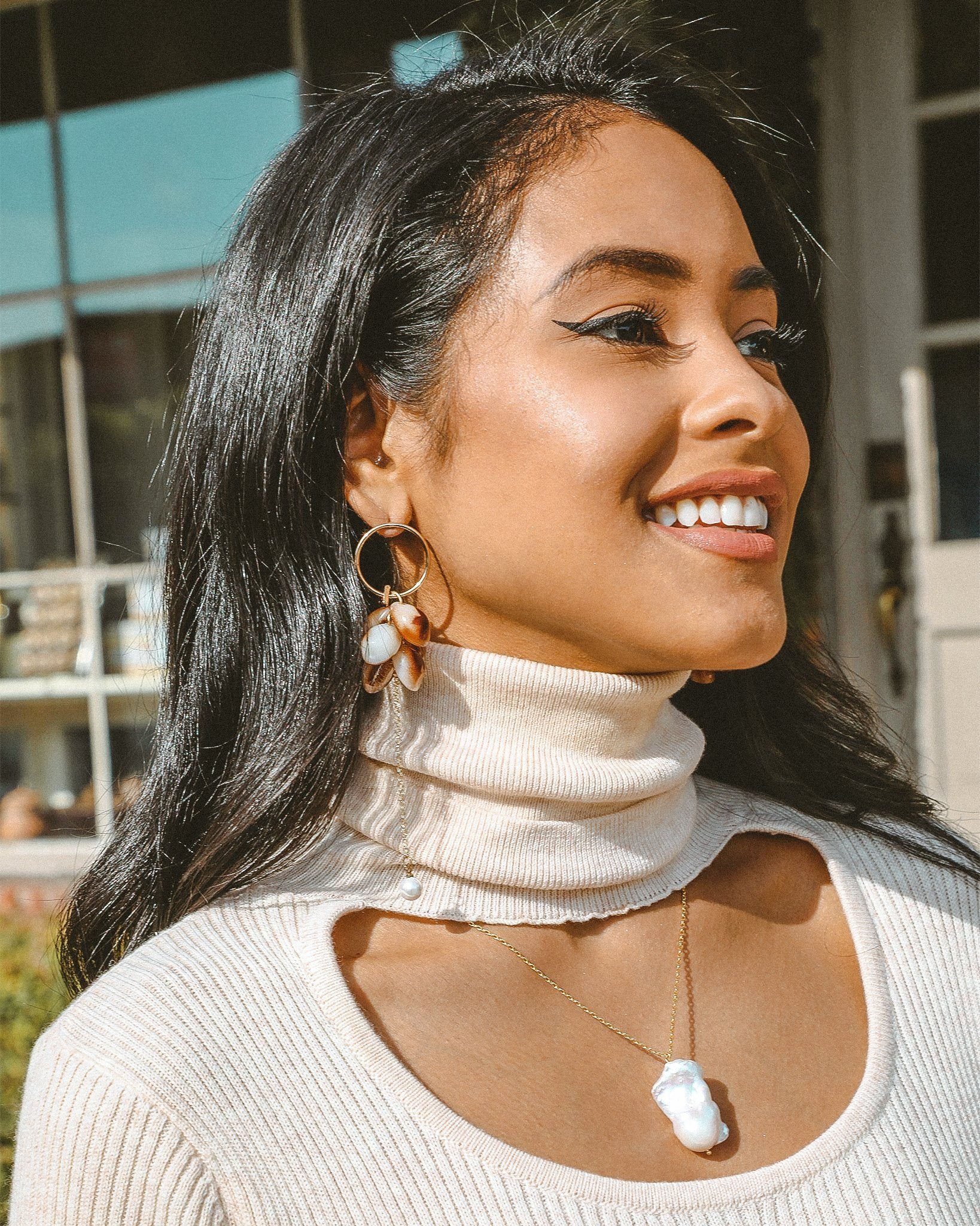 Beautiful woman wearing a white turtleneck sweater with hoop earrings and a necklace standing outdoors